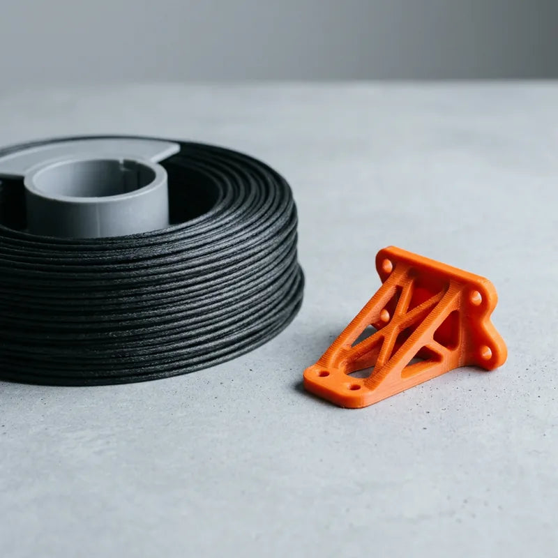 Black carbon-fiber nylon coil beside an orange printed structural gusset