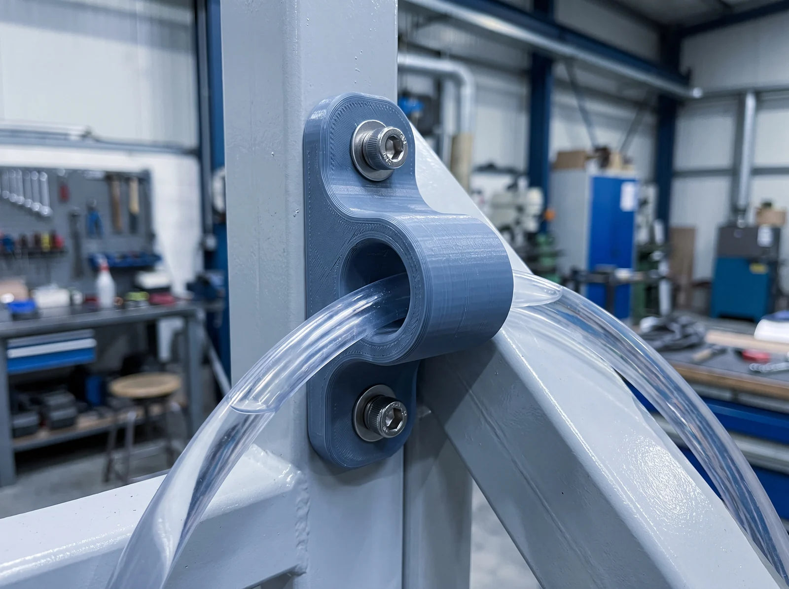 A 3D-printed bracket bolted to a painted steel frame in a workshop, with clear fluid tubing running through it